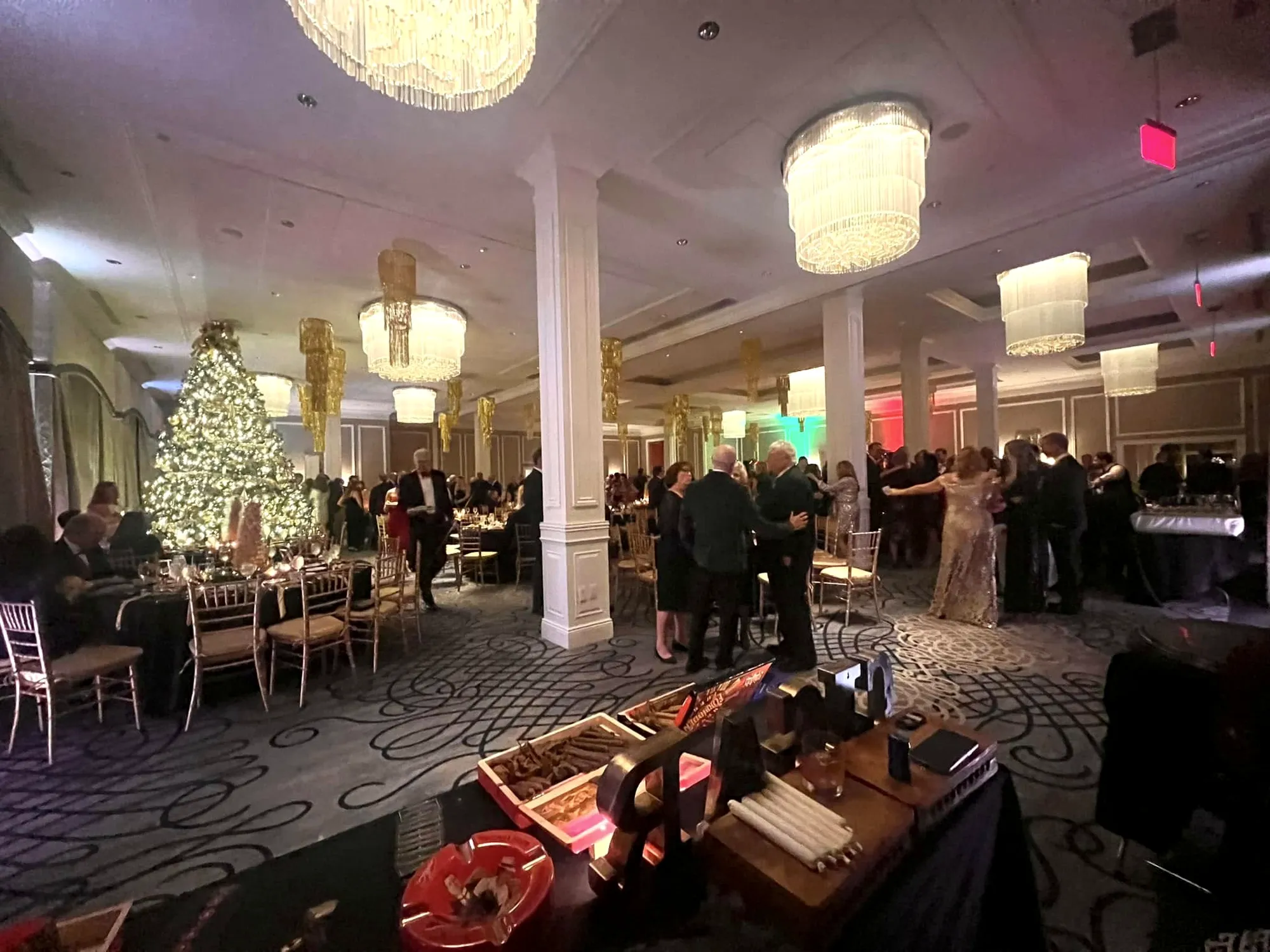 A country club ballroom at Christmas, black-tie guests behind and his rolling table in front