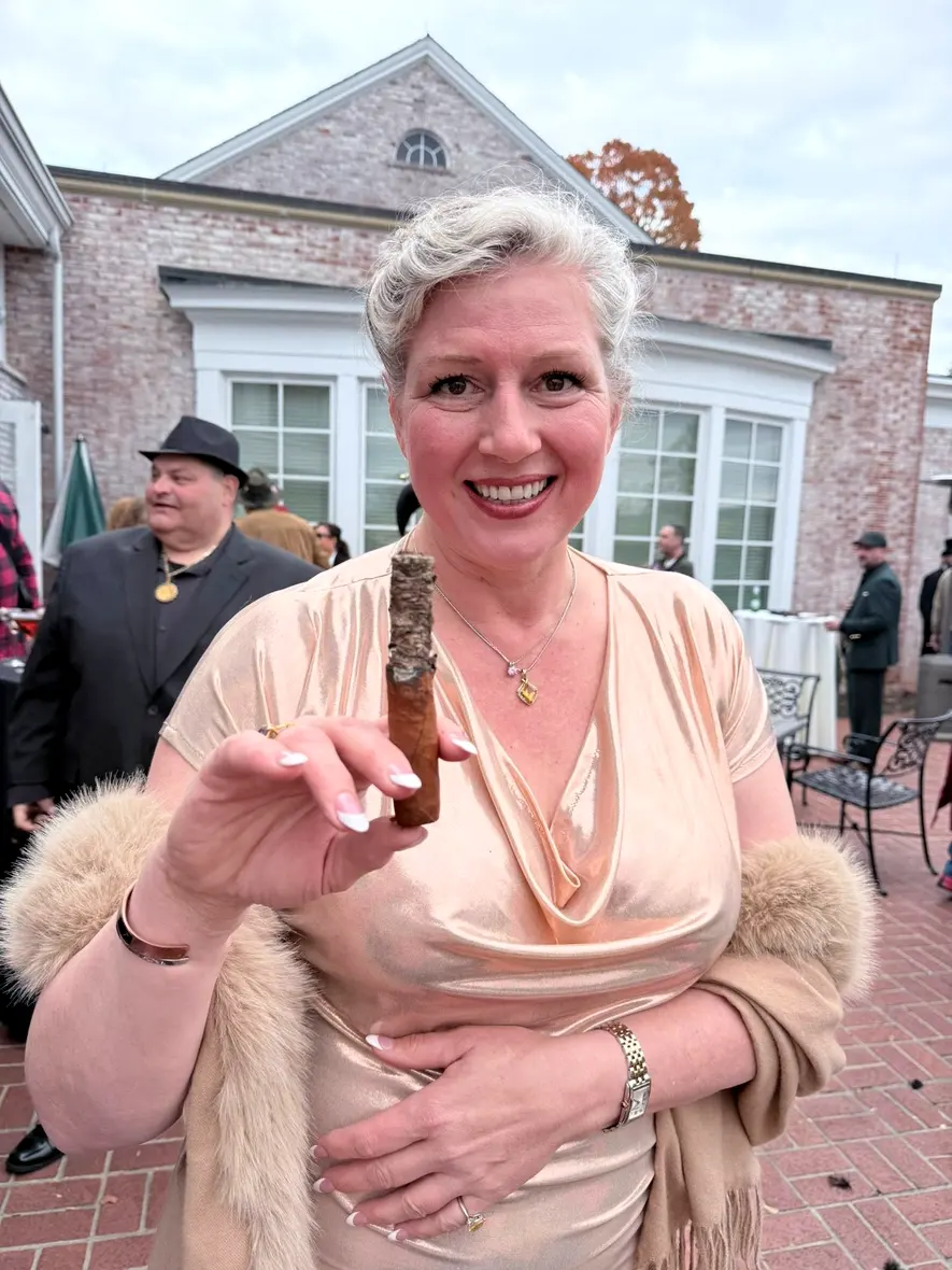 A guest in a gold gown smiling with the cigar he just rolled for her