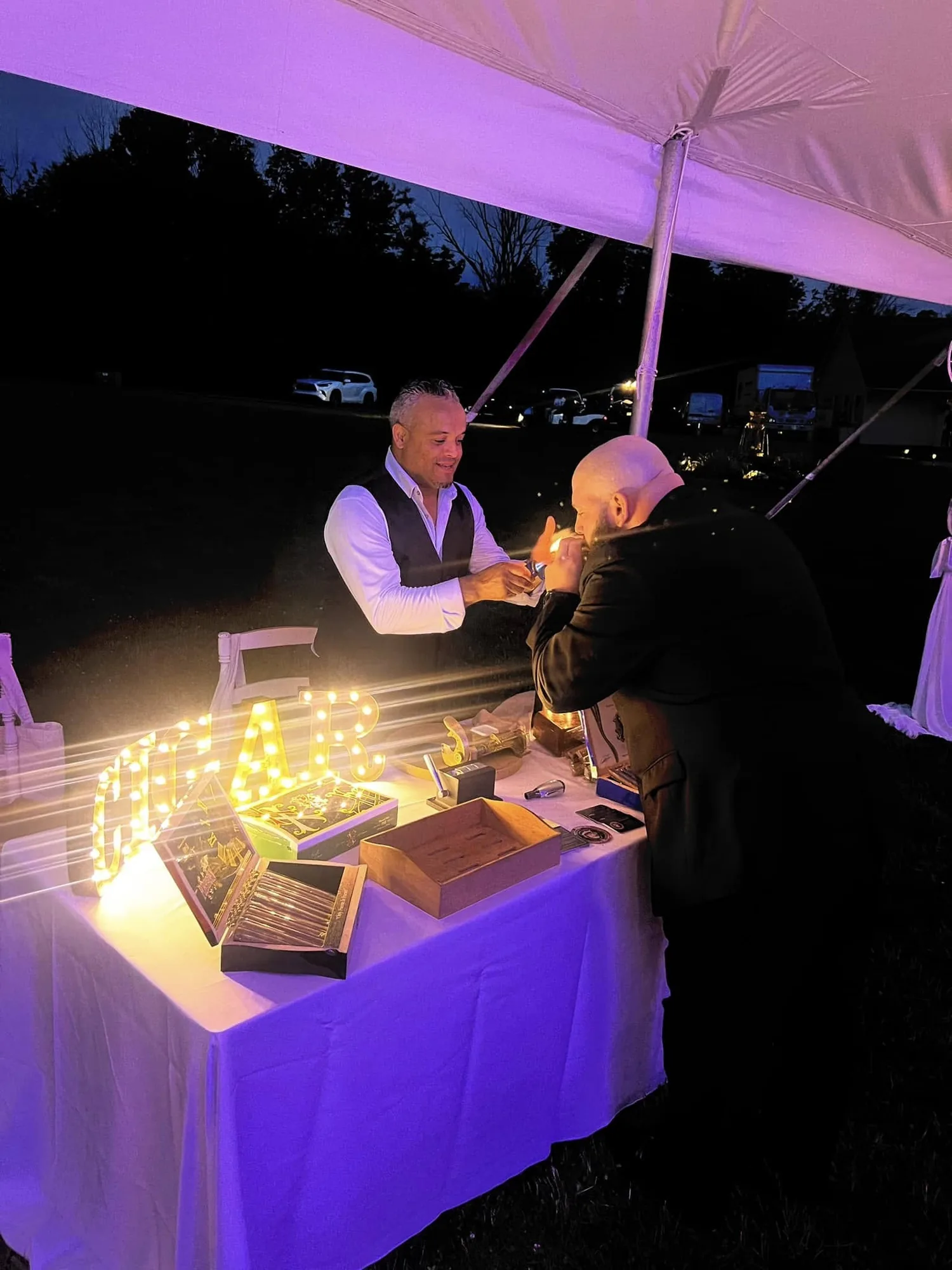 Franklin Pichardo still rolling at his table under a wedding tent late at night, as a guest lights a cigar