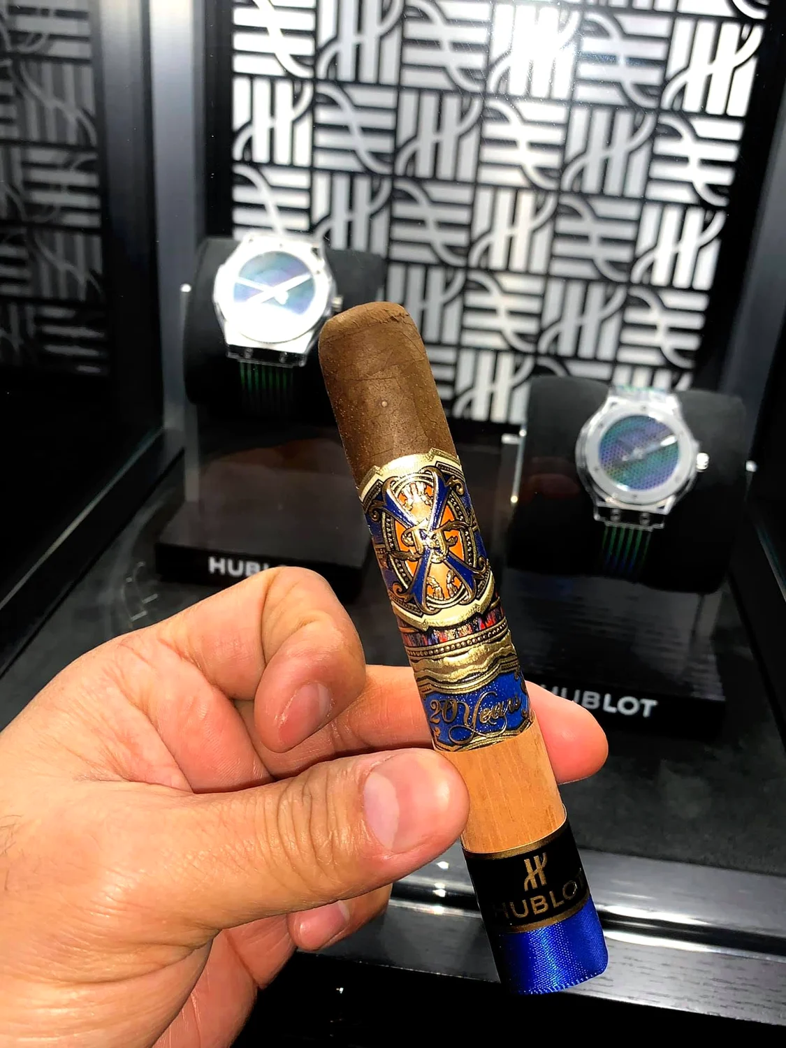 One of his cigars with the blue Hublot band, in front of the watches on display