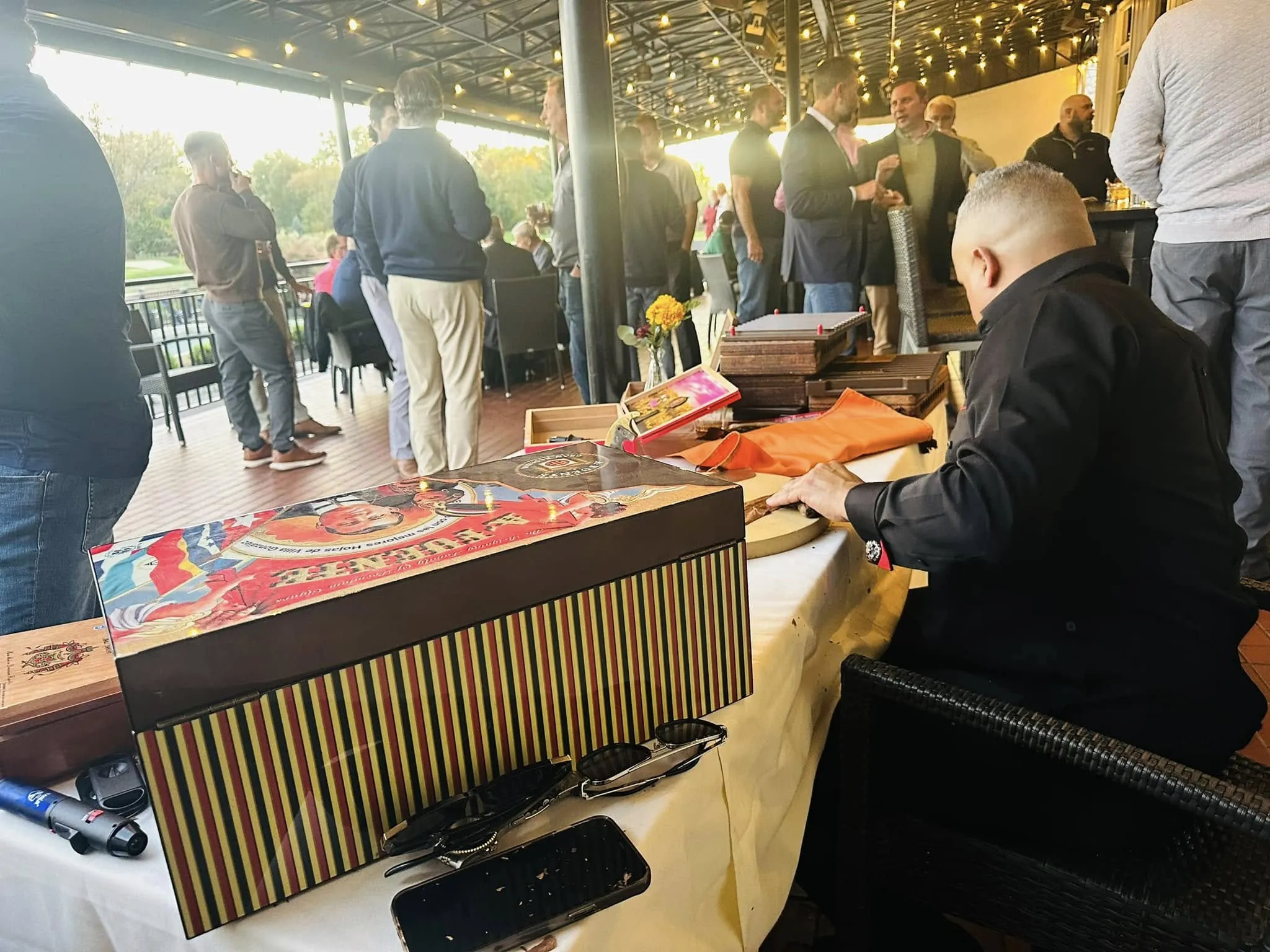 Franklin rolling at his table under string lights on a covered terrace, guests standing and talking behind him